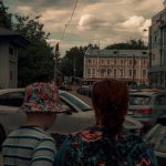 a couple of women standing in a parking lot with cars and buildings