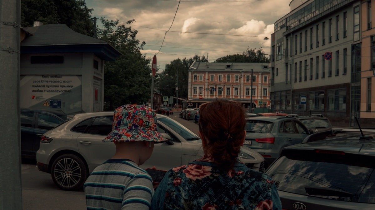 a couple of women standing in a parking lot with cars and buildings
